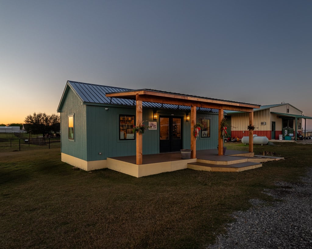 Lydia's Boutique & Yarn at Goshen Meadows at sunset, a teal 14x32 cabin shell with a black metal roof and a covered front porch